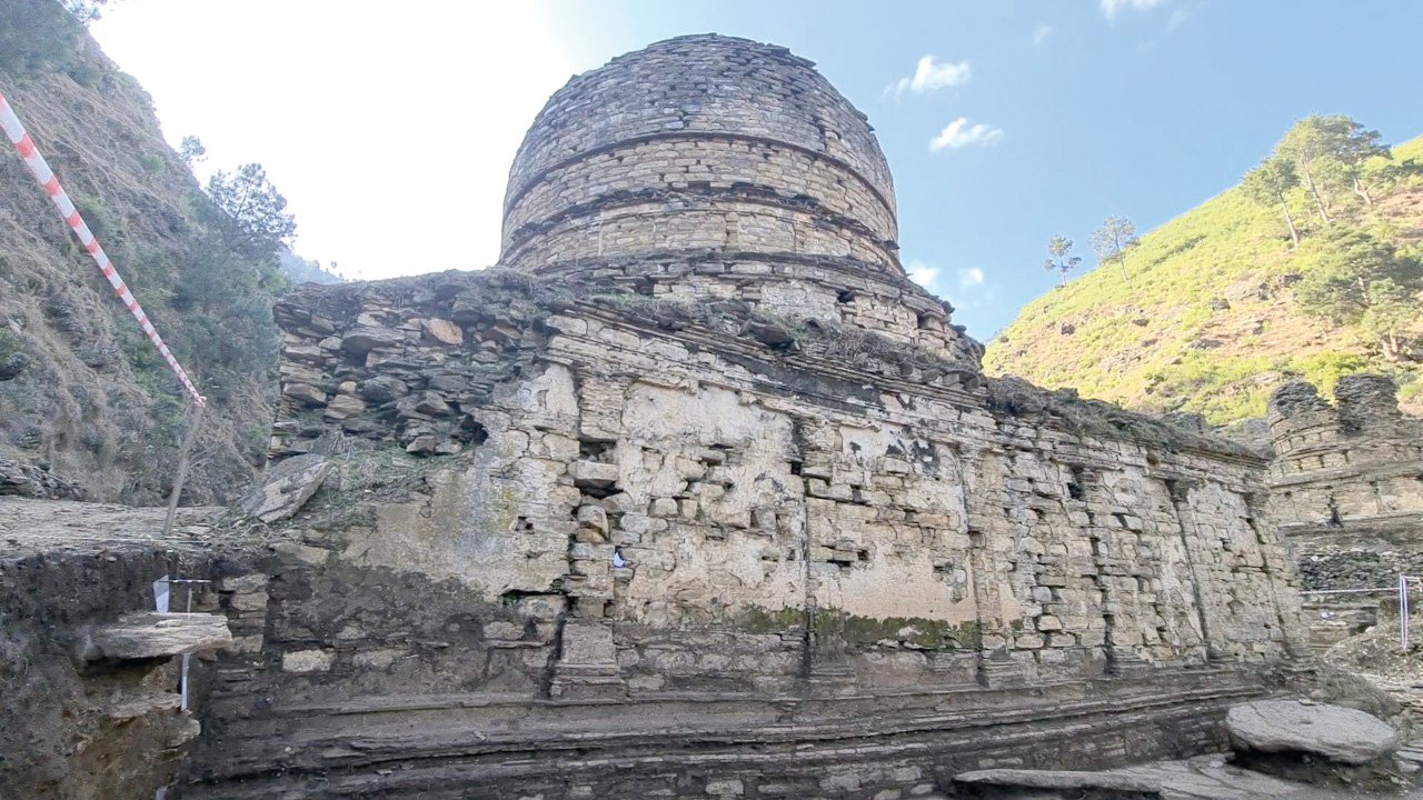  The image shows the preserved ruins of a Buddhist temple complex with a large stone stupa, smaller stupas, and stone walls, with a mountain in the background.